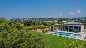 A modern house with a swimming pool, a covered outdoor seating area, and a view of the surrounding landscape.