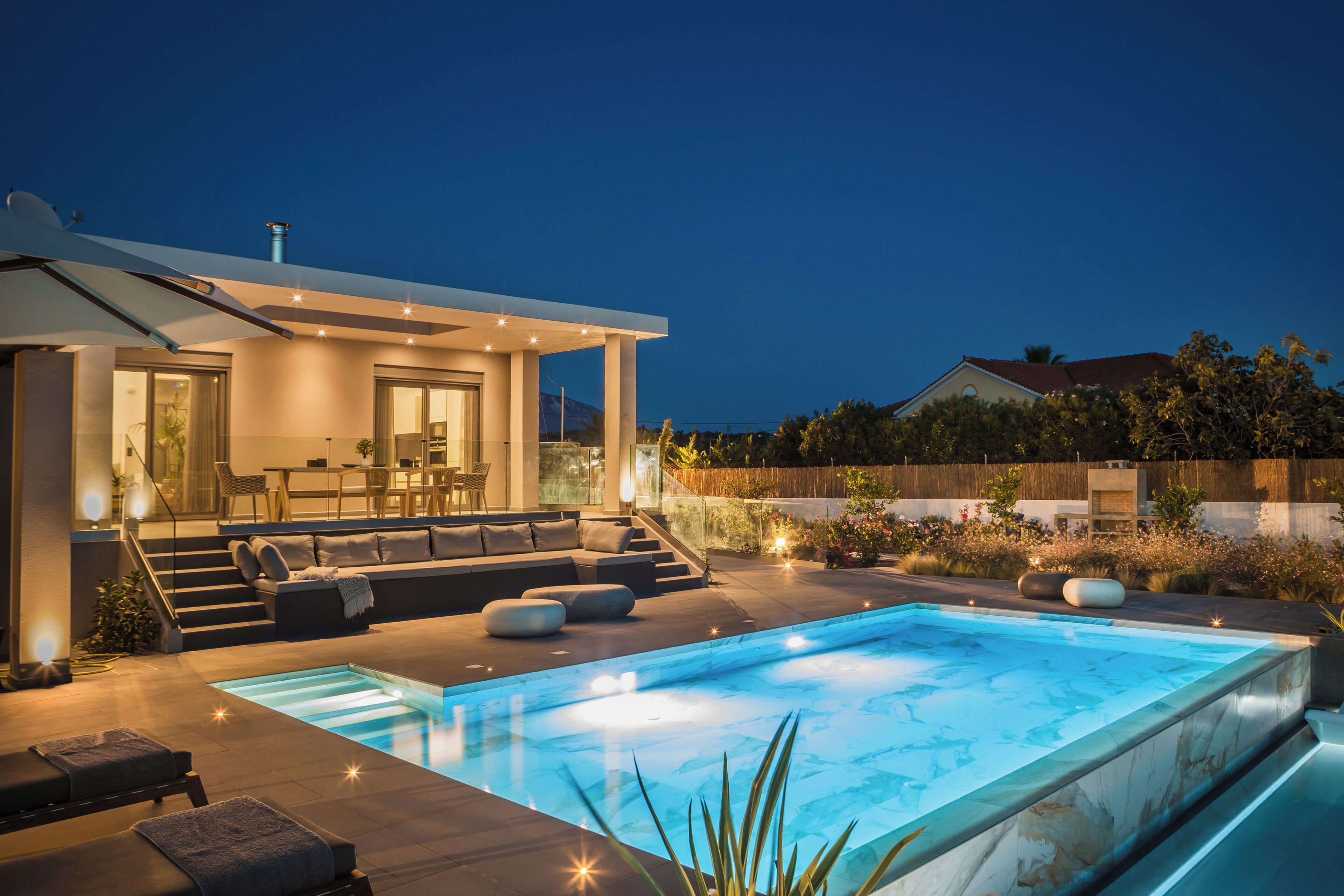 A modern house with a swimming pool, outdoor seating, and a staircase leading to a deck.