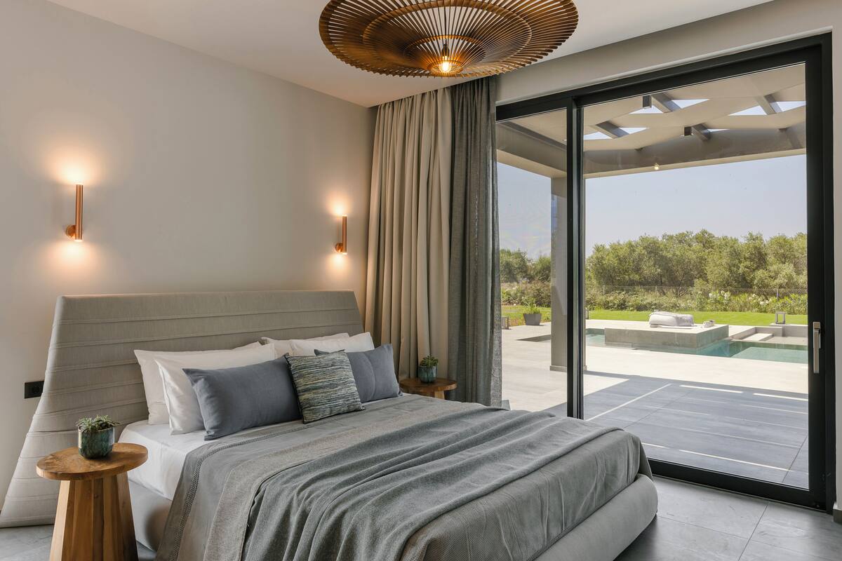 A modern bedroom with a large bed, a view of a pool, and a ceiling light fixture.