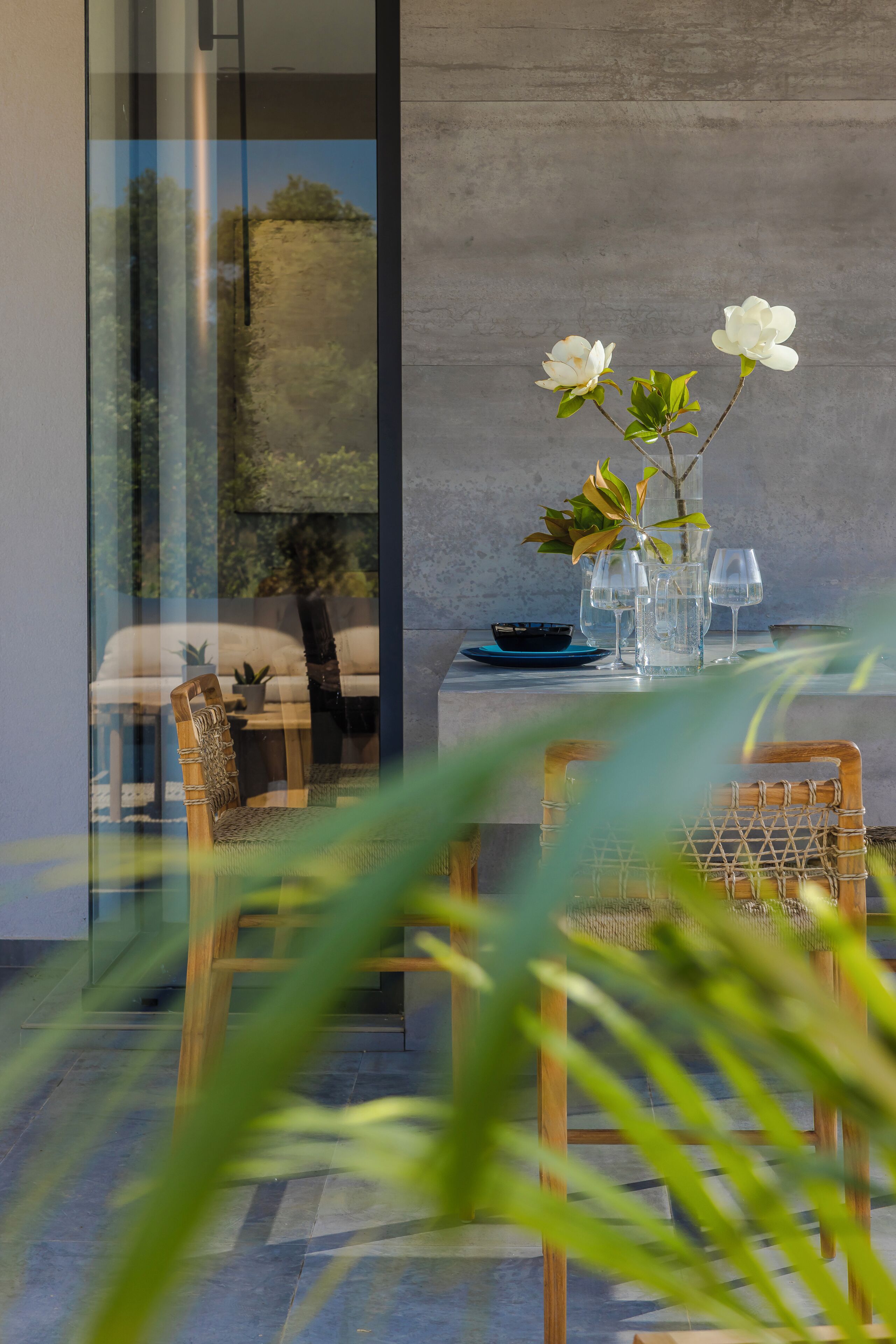 Una mesa de comedor con sillas, un jarrón con flores y vistas a través de un ventanal.