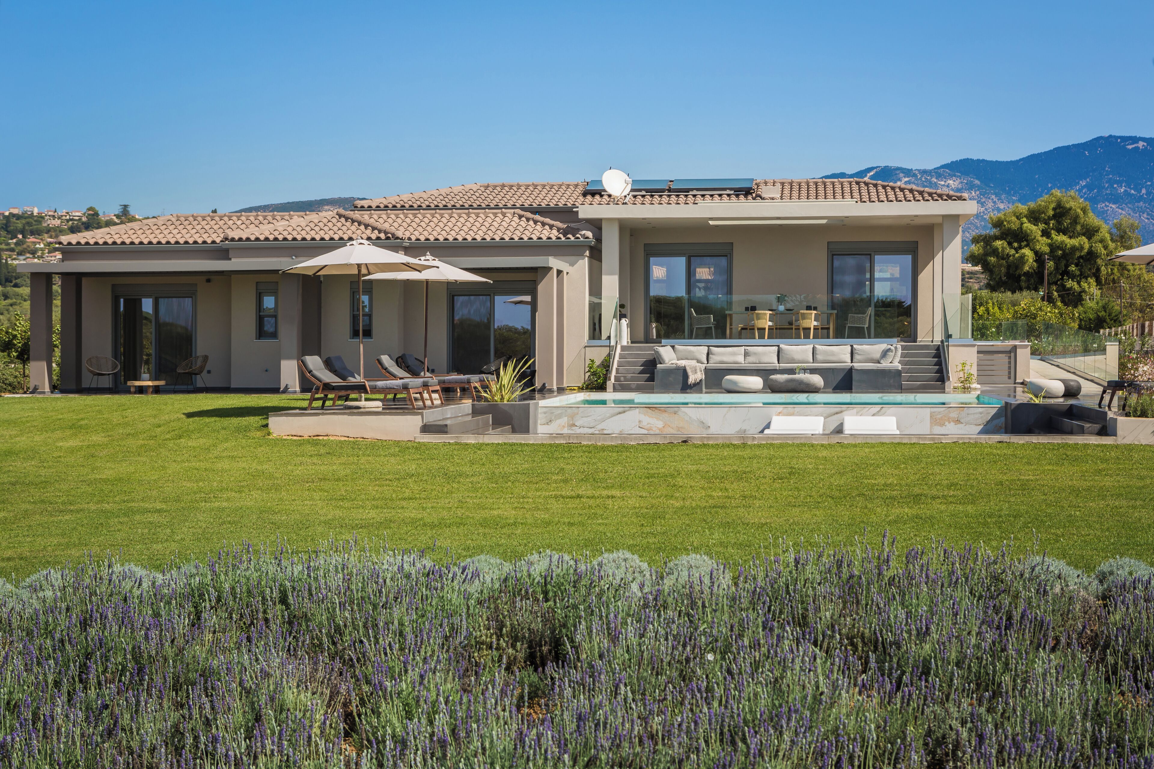 A modern house with a swimming pool, outdoor seating, and a view of the mountains.