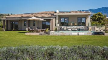 A modern house with a swimming pool, outdoor seating, and a view of the mountains.
