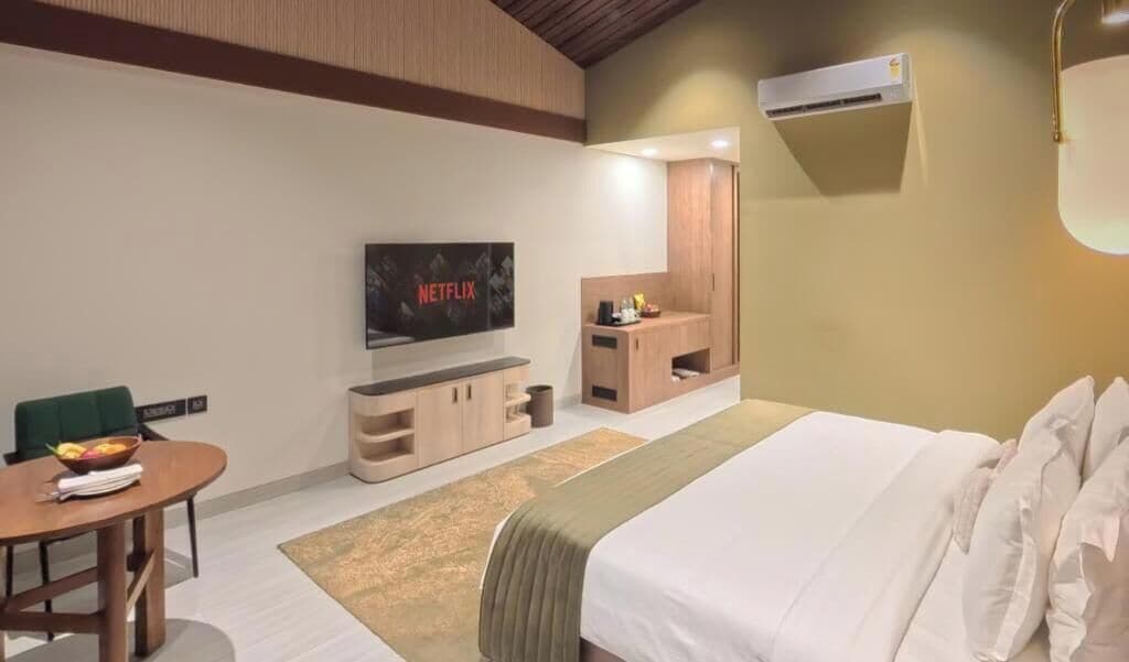 Ein modernes Hotelzimmer mit Bett, Fernseher, Schreibtisch und einer kleinen Sitzecke.