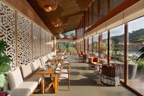 A spacious indoor area with seating arrangements, large windows, and a view of the outdoors. - Miros Neral - Foothills of Matheran (Karjat)