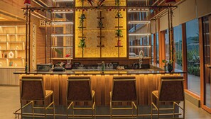 A bar area with wooden bar counter, three bar stools, and shelves with decorative items. - Celebration Land by Miros (Karjat)