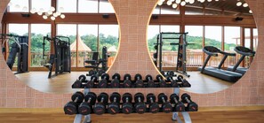 A gym with exercise equipment, a treadmill, and a view of greenery through large windows. - Celebration Land by Miros (Karjat)