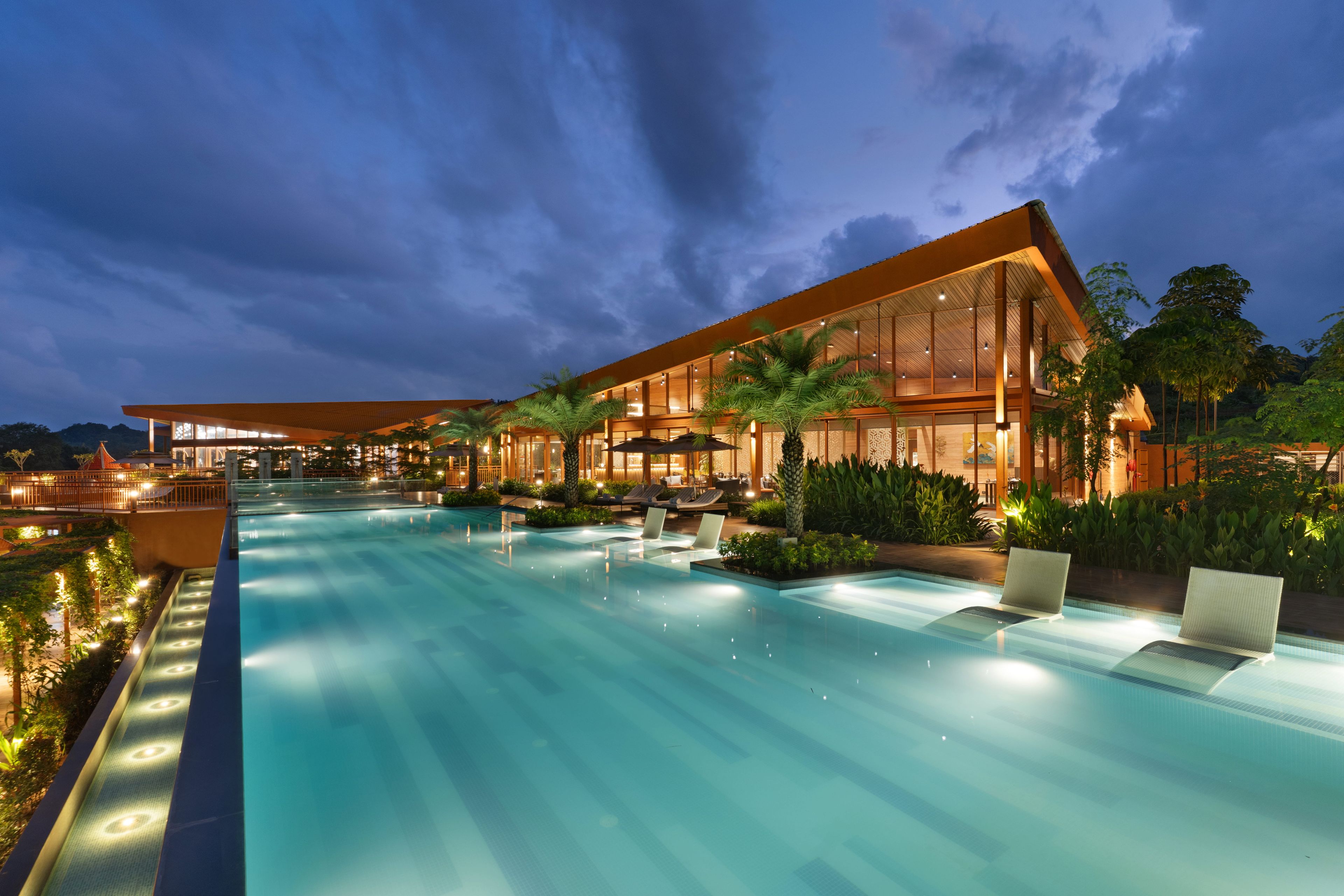 Un hôtel moderne doté d’une grande piscine extérieure, d’espaces de détente et d’une façade bien éclairée.
