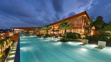 Un hotel moderno con una amplia piscina exterior, zonas de descanso y una fachada de edificio bien iluminada.