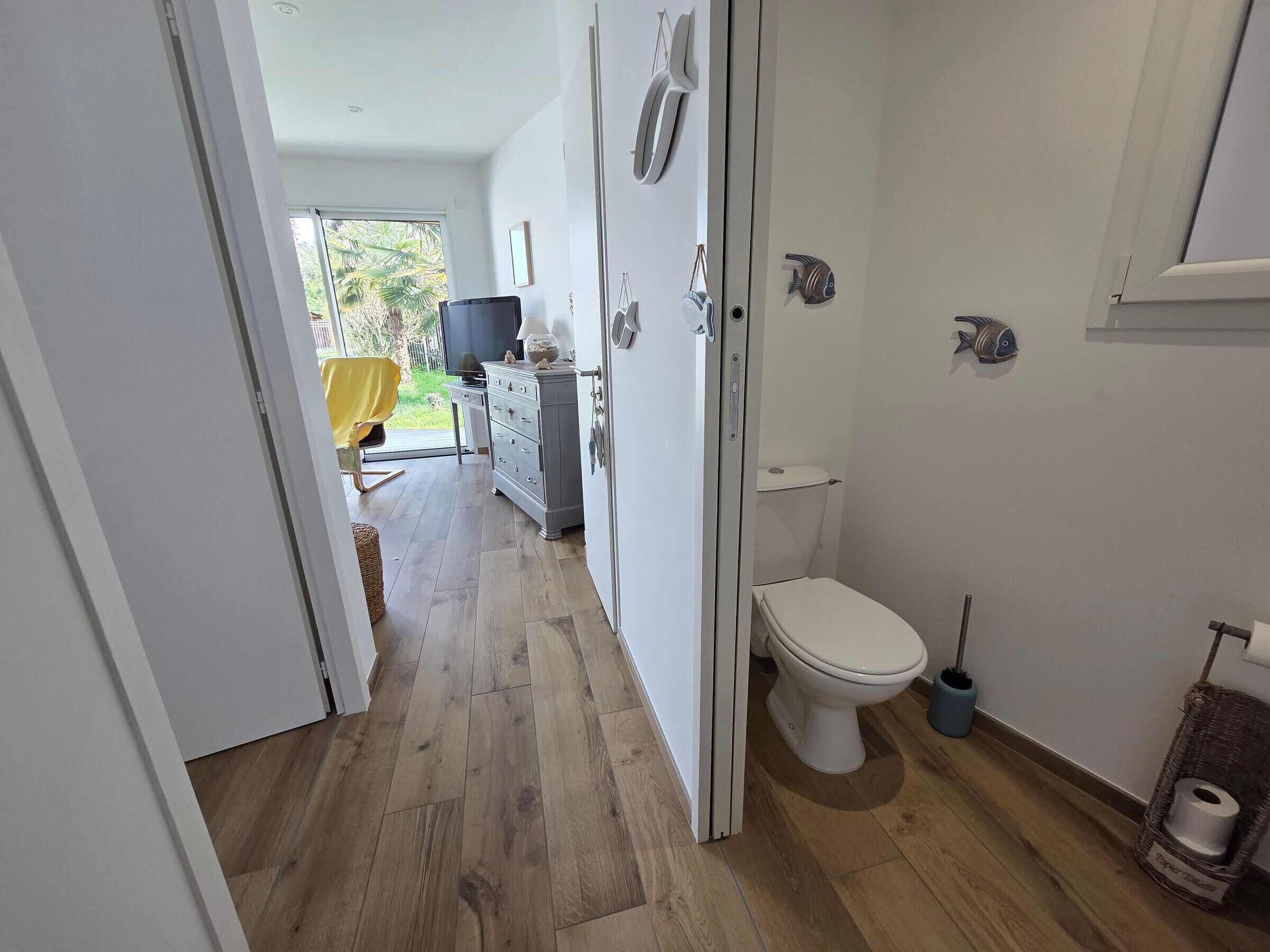 Une salle de bain avec des toilettes, un lavabo et un miroir. On y trouve un panier en osier contenant un rouleau de papier toilette.