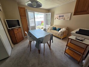 A room with a dining table, chairs, a sofa, a television, and a small table with a tray. - House near the beach - 4 guests (La Tranche-sur-Mer)