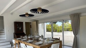 A dining area with a wooden table set for six, white chairs, and two pendant lights. - Comfortable house, pets welcome - 10 guests (Noirmoutier-en-l'Île)