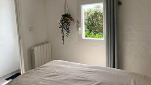 A bedroom with a bed, a window, a radiator, and a hanging plant. - Comfortable house, pets welcome - 10 guests (Noirmoutier-en-l'Île)