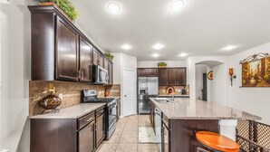 A modern kitchen with dark wood cabinets, stainless steel appliances, and a granite countertop. - Cypress - Private Bedroom in Shared Home (Cypress)