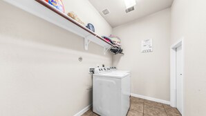 A laundry room with a washing machine, a shelf with laundry supplies, and a door. - Cypress - Private Bedroom in Shared Home (Cypress)