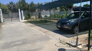 Pysäköintialue, jossa on auto, portilla varustettu sisäänkäynti ja katettu alue, jossa on valaisinpylväs.