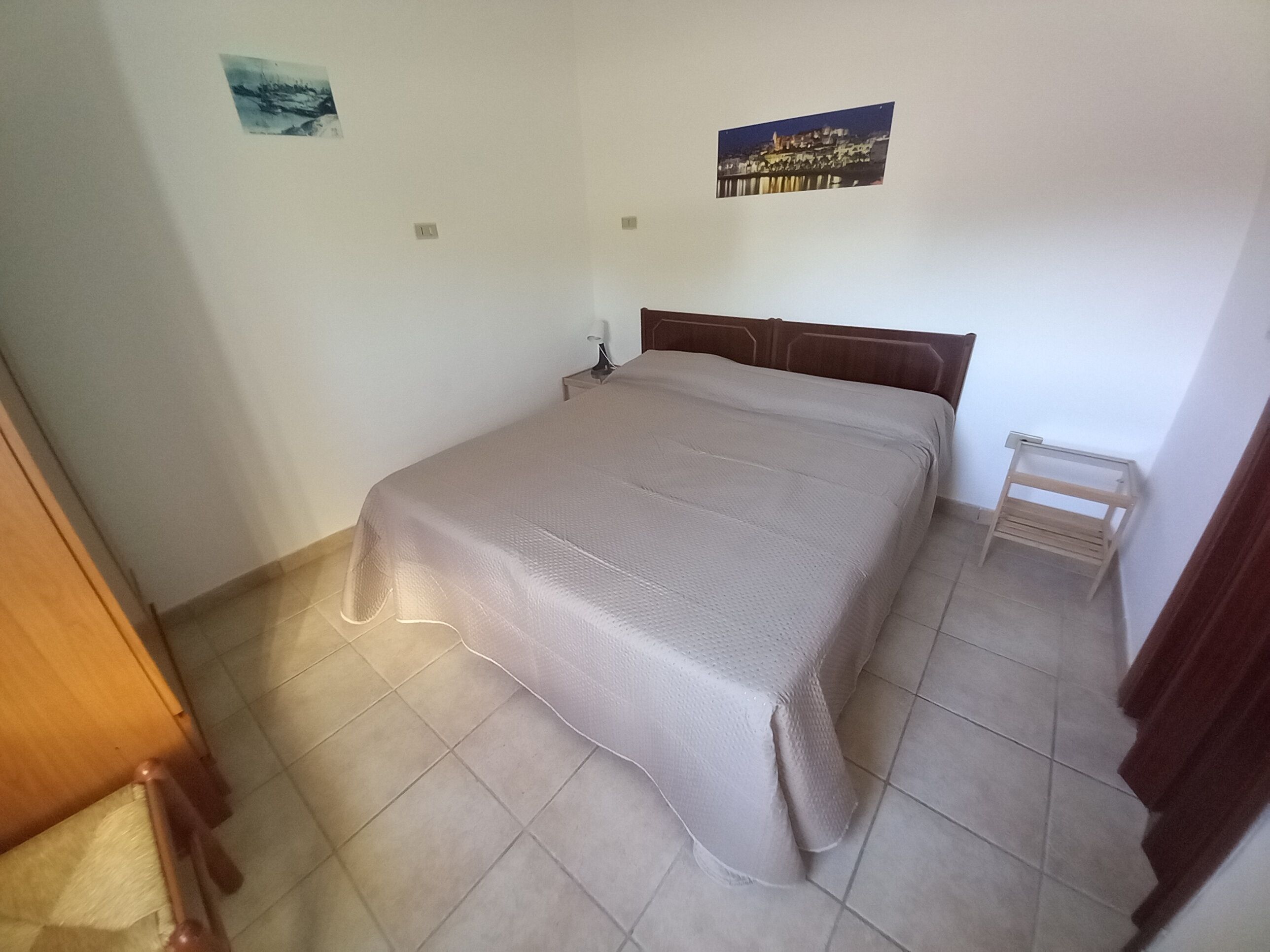 Quarto com uma cama, uma mesa de cabeceira, uma mesinha e duas imagens penduradas na parede.
