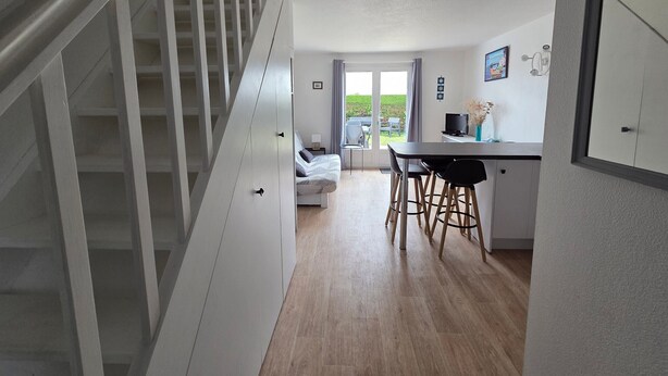 A modern interior with a staircase, a kitchen area with bar stools, and a dining table.