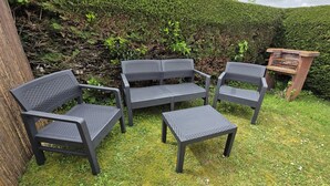 A garden with a seating area consisting of two chairs, a table, and a small wooden structure.
