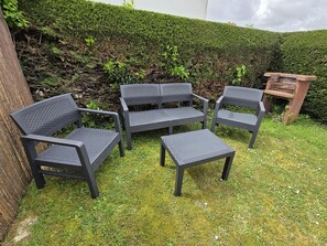 Un jardin agrémenté d’un espace détente composé de deux chaises, d’une table et d’une petite structure en bois.
