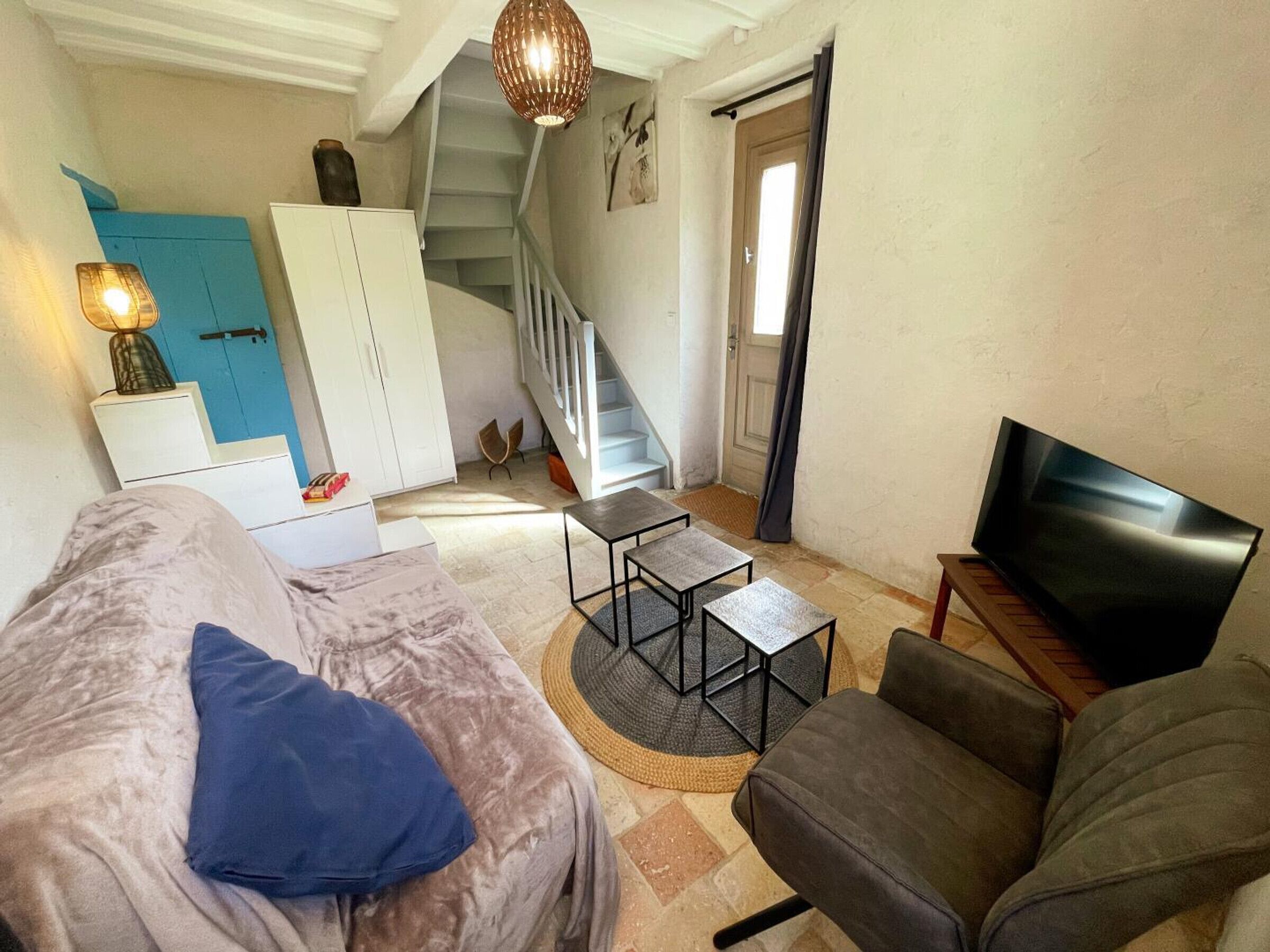 A living room with a sofa, armchair, coffee table, TV, staircase, and a door.