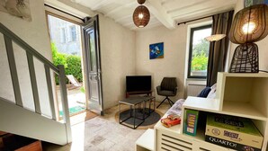 A living room with a TV, a chair, a bookshelf, and a staircase. - Historic charm cottage - 3 guests (Sazilly)
