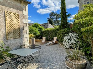 Eine Terrasse mit Tisch und Stühlen, umgeben von Kies und Grünpflanzen.