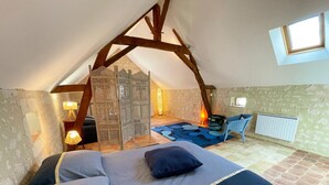 A bedroom with a sloped ceiling, a bed with pillows, a chair, a table, and a window. - Historic charm cottage - 3 guests (Sazilly)