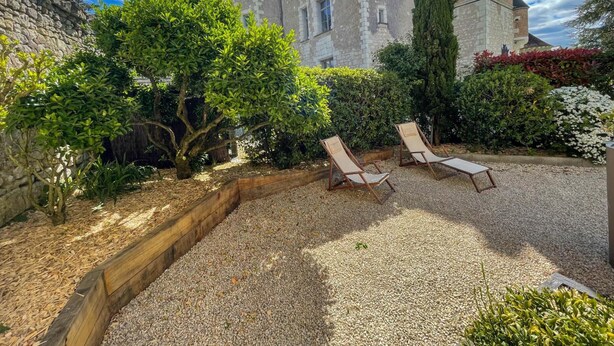 A courtyard with a stone wall, two lounge chairs, and a building with a tower. - Historic charm cottage - 3 guests (Sazilly)