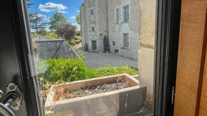 A stone building with a turret, a window with a view of a courtyard, and a planter box with plants. - Historic charm cottage - 3 guests (Sazilly)