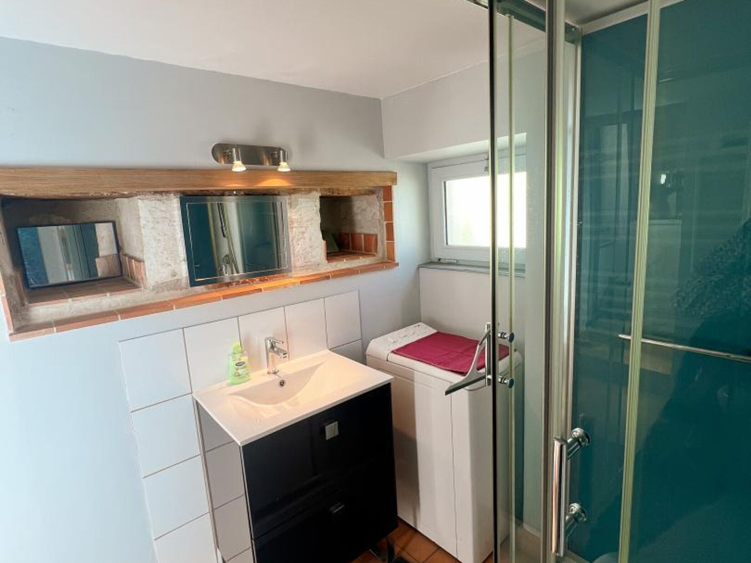 A compact bathroom with a glass shower enclosure, a small sink, and a mirror above it.