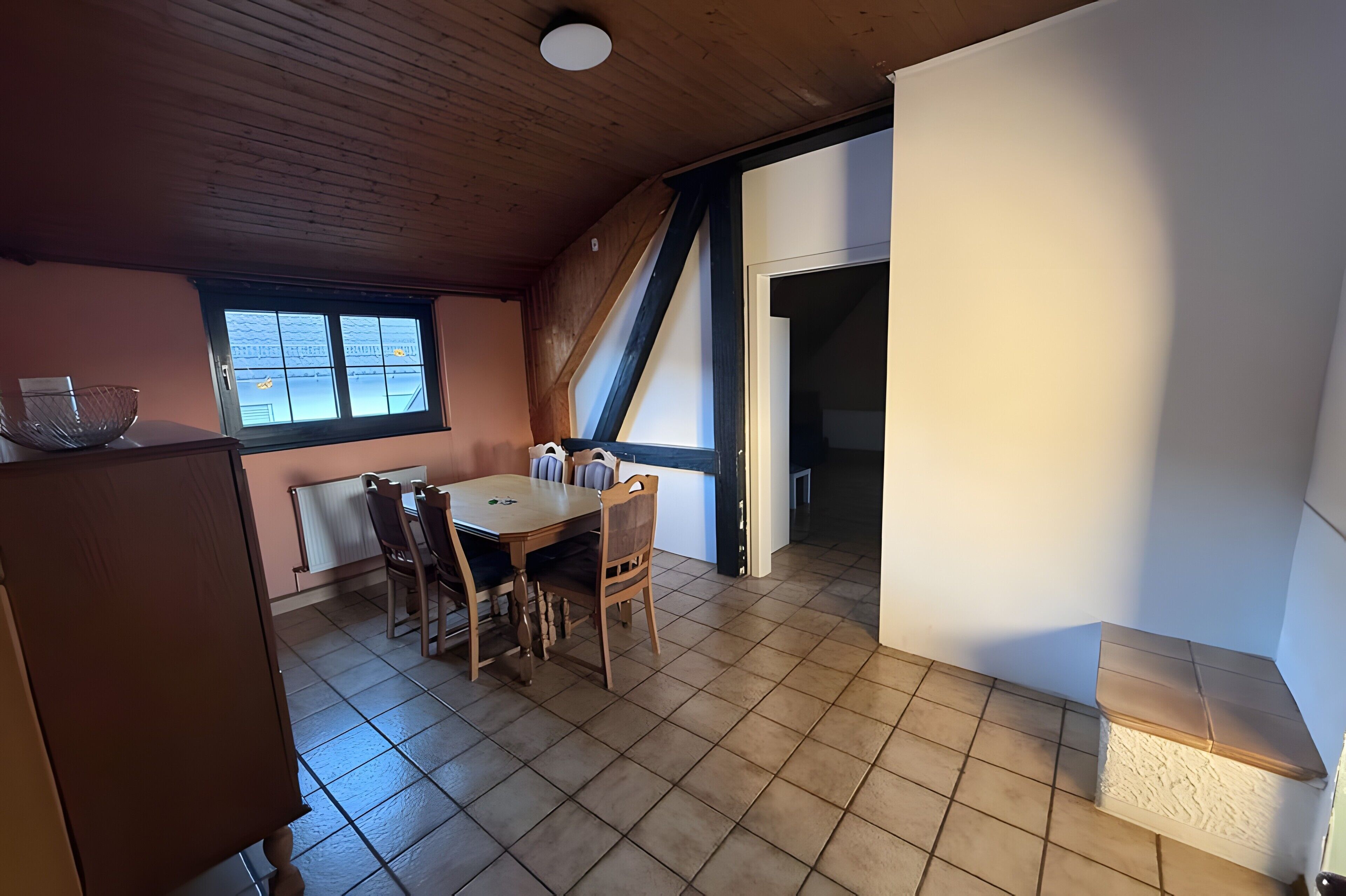 Un comedor con una mesa y sillas de madera, una ventana con vistas, y una escalera que sube a otro nivel.