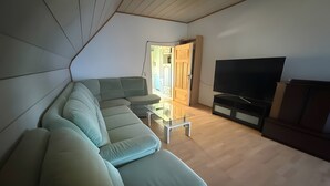 A living room with a sectional sofa, a glass coffee table, a flat-screen TV, and a wooden cabinet. - Spacious & Comfortable House – Perfect for Workers or Holiday Guests (Orbis)