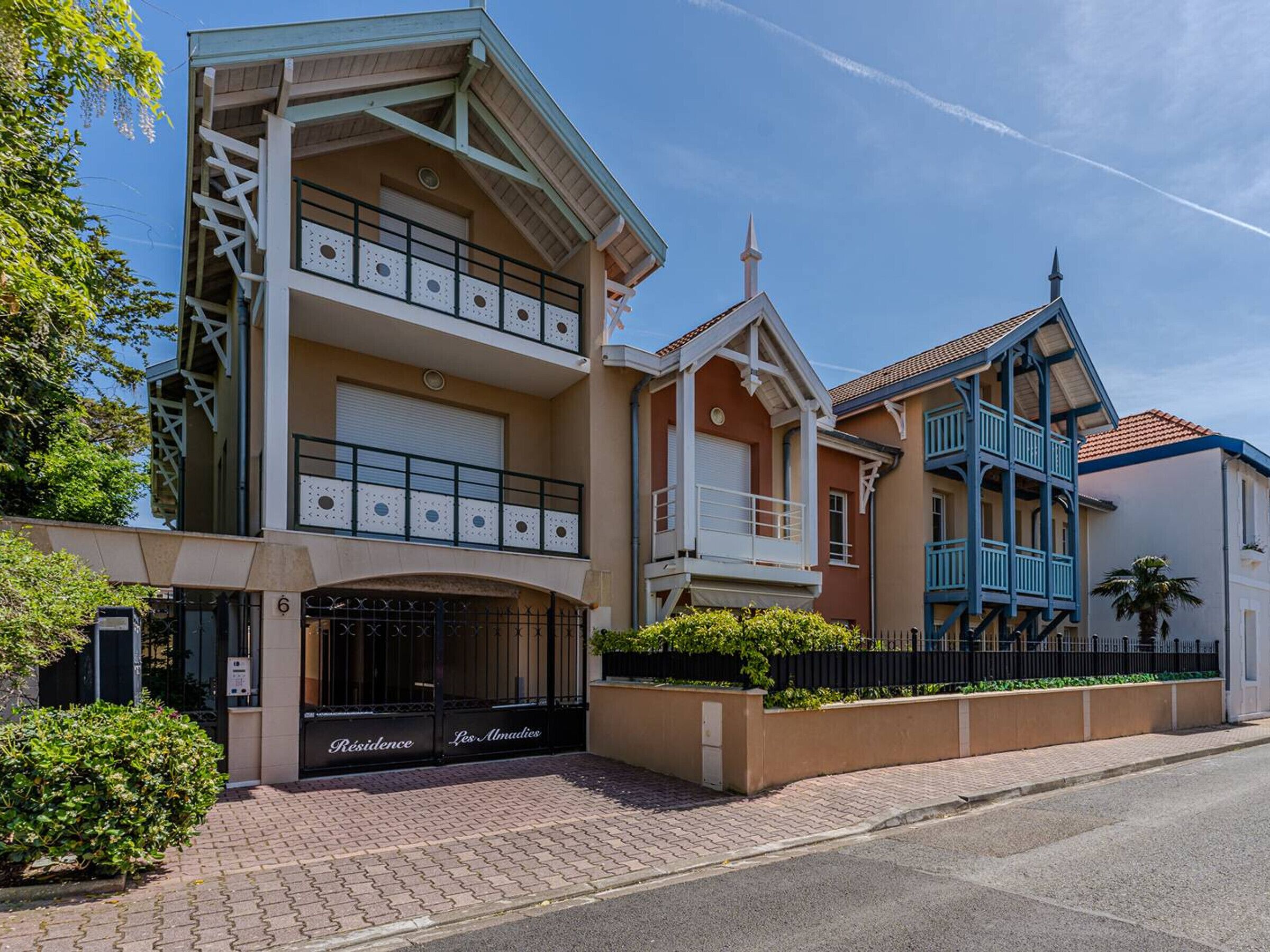 A multi-story residential building with a gated entrance, balconies, and a clear sky.