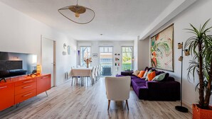 Een moderne woonkamer met een televisie, oranje kasten, een paarse bank en een eethoek.