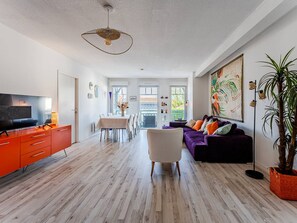 Un salon moderne avec un téléviseur, des meubles de rangement orange, un canapé violet et un coin repas.