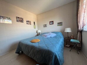 A bedroom with a bed, two bedside tables, a lamp, and a window with curtains. - Spacious apartment with ocean view - 4 guests (Vaux-sur-Mer)