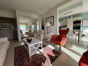 A spacious living room with a large mirror, a red armchair, a white coffee table, and a patterned rug. - Spacious apartment with ocean view - 4 guests (Vaux-sur-Mer)