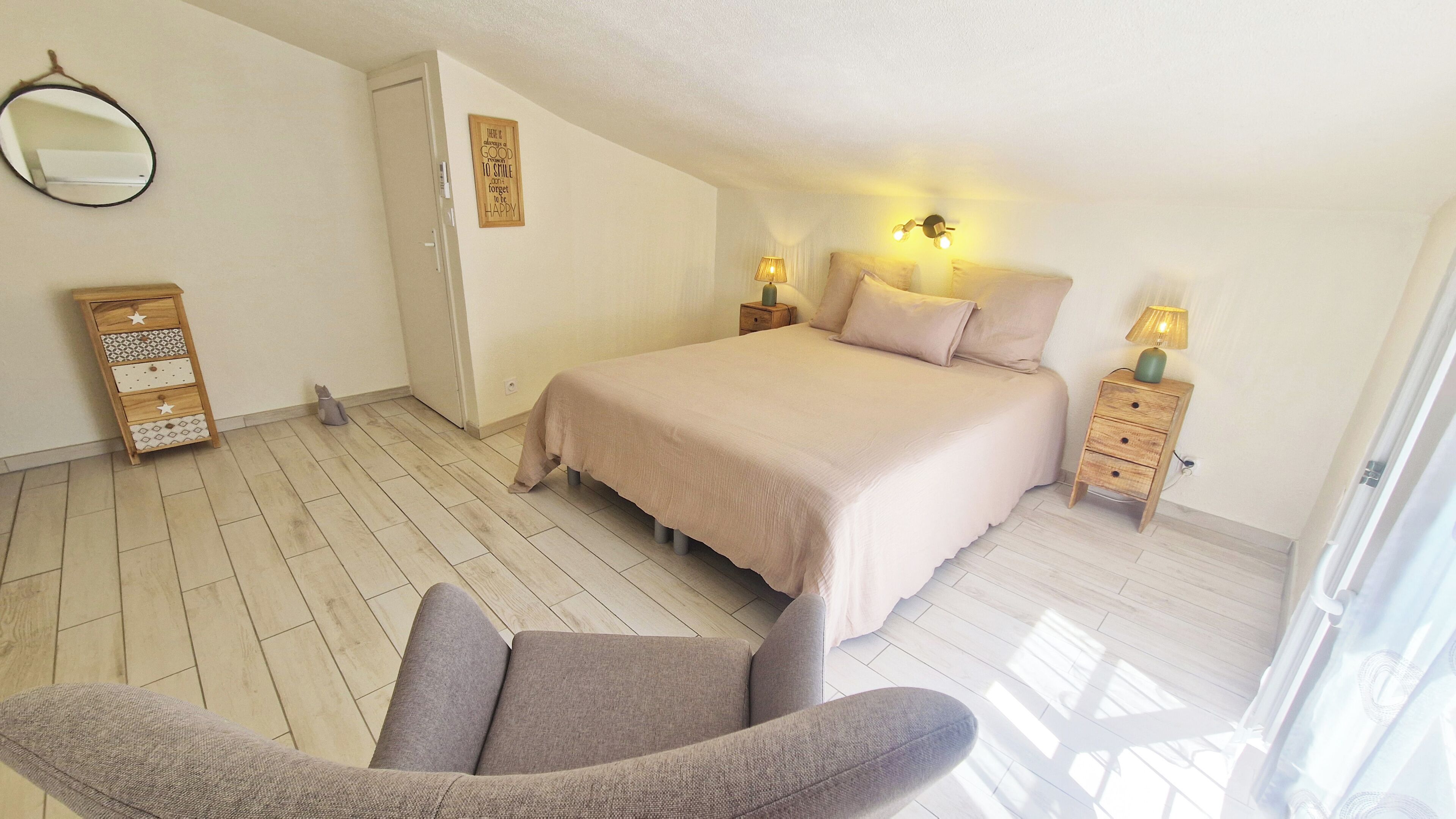 Ein Schlafzimmer mit Bett, Nachttischen, einem Sessel, einer Kommode und einem Spiegel.