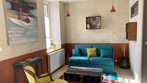 Una sala de estar con un sofá azul, un sillón amarillo, un baúl antiguo, un radiador y un cartel en la pared.