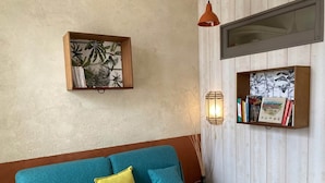 Una habitación con un sofá azul, una estantería de madera y una lámpara fijada a la pared.