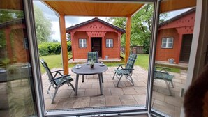 A glass-enclosed patio with a table and chairs, a small house in the background, and a grassy area.