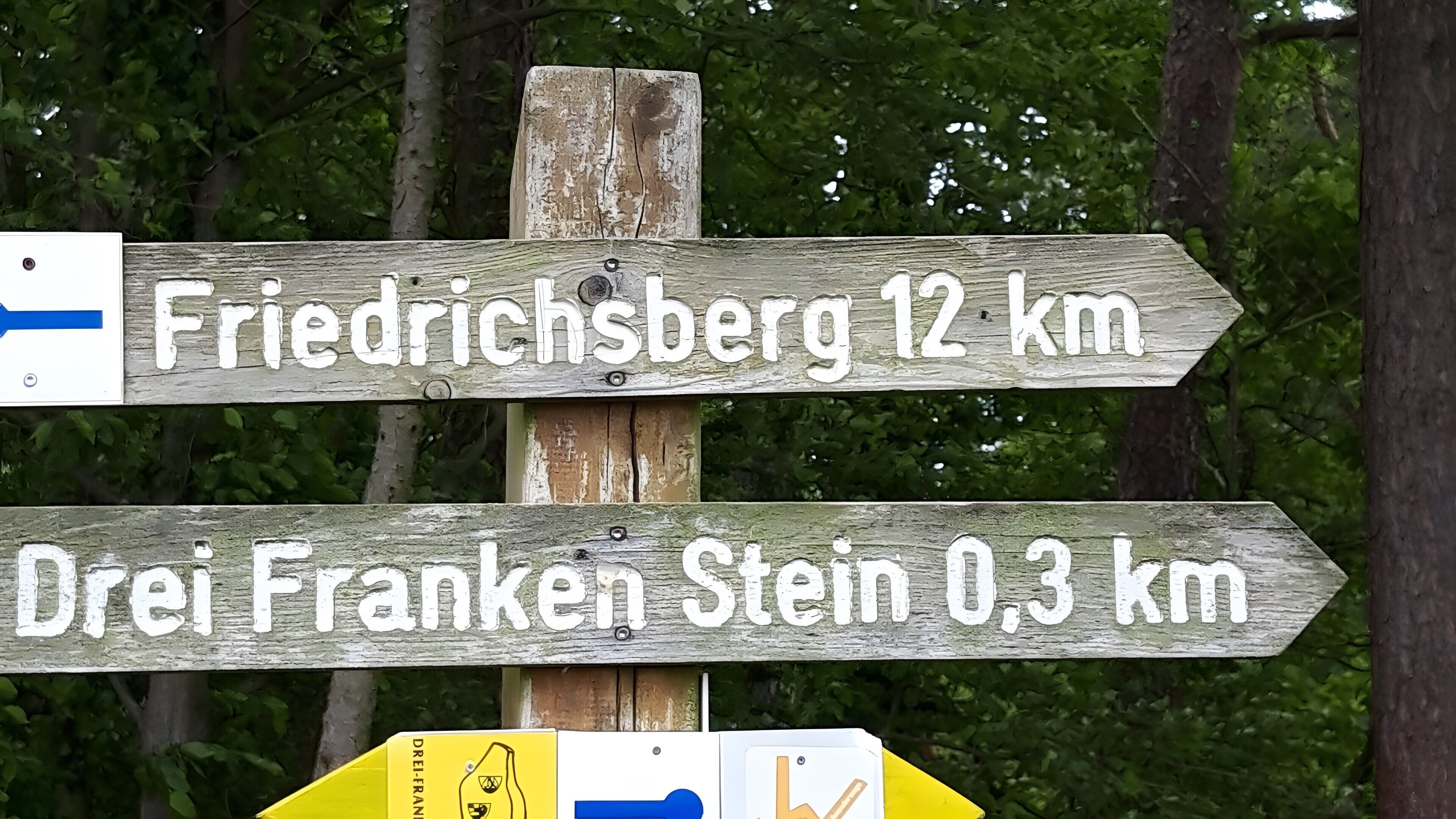 Un cartel de madera señala Friedrichsberg a 12 km y Drei Franken Stein a 0.3 km.