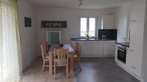 A modern kitchen with white cabinets, a dining table with chairs, a window, and a built-in oven.