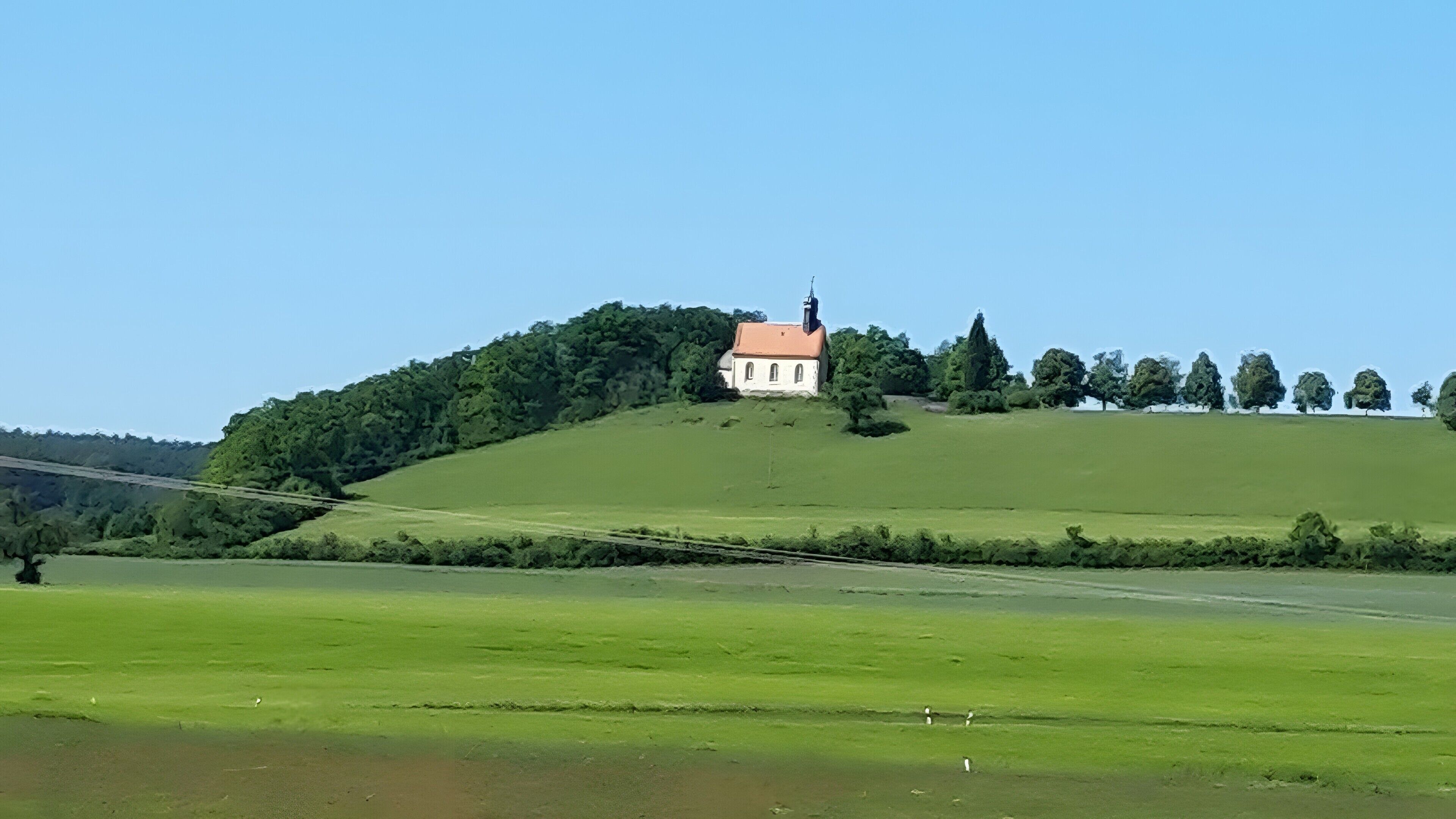 A rural landscape with a single building on a hill, surrounded by greenery and trees.