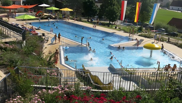 A swimming pool with multiple lanes, surrounded by a fence, and a water slide.
