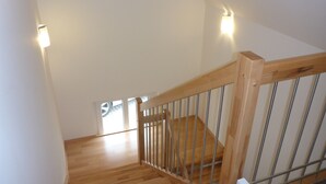 Eine Holztreppe mit Metallgeländern, weißen Wänden und zwei Wandleuchten.
