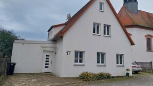 Ein zweistöckiges Haus mit weißer Fassade, einem roten Ziegeldach und einem kleinen, turmartigen Aufbau auf dem Dach.