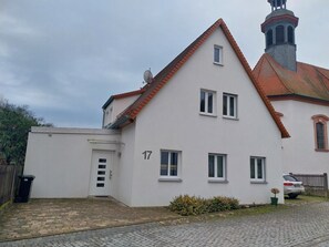 Ein zweistöckiges Haus mit weißer Fassade, einem roten Ziegeldach und einem kleinen, turmartigen Aufbau auf dem Dach.