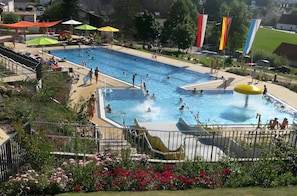 A swimming pool with multiple lanes, a water slide, and a fenced area with flowers. - Cozy Apartment in the Historic Center of Schlüsselfeld (Schlüsselfeld)