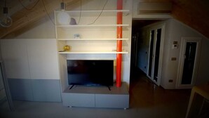 A room with a built-in entertainment unit, a white cabinet, and a red accent piece. - Attic Boutique May (Bergamo)